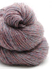 A close-up of a skein of variegated yarn with a heathered texture in dusty rose, mauve, and muted blue tones, set against a clean white background.