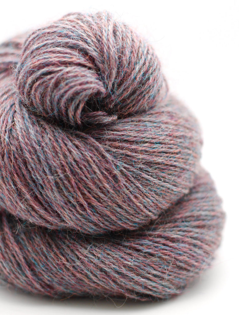 A close-up of a skein of variegated yarn with a heathered texture in dusty rose, mauve, and muted blue tones, set against a clean white background.