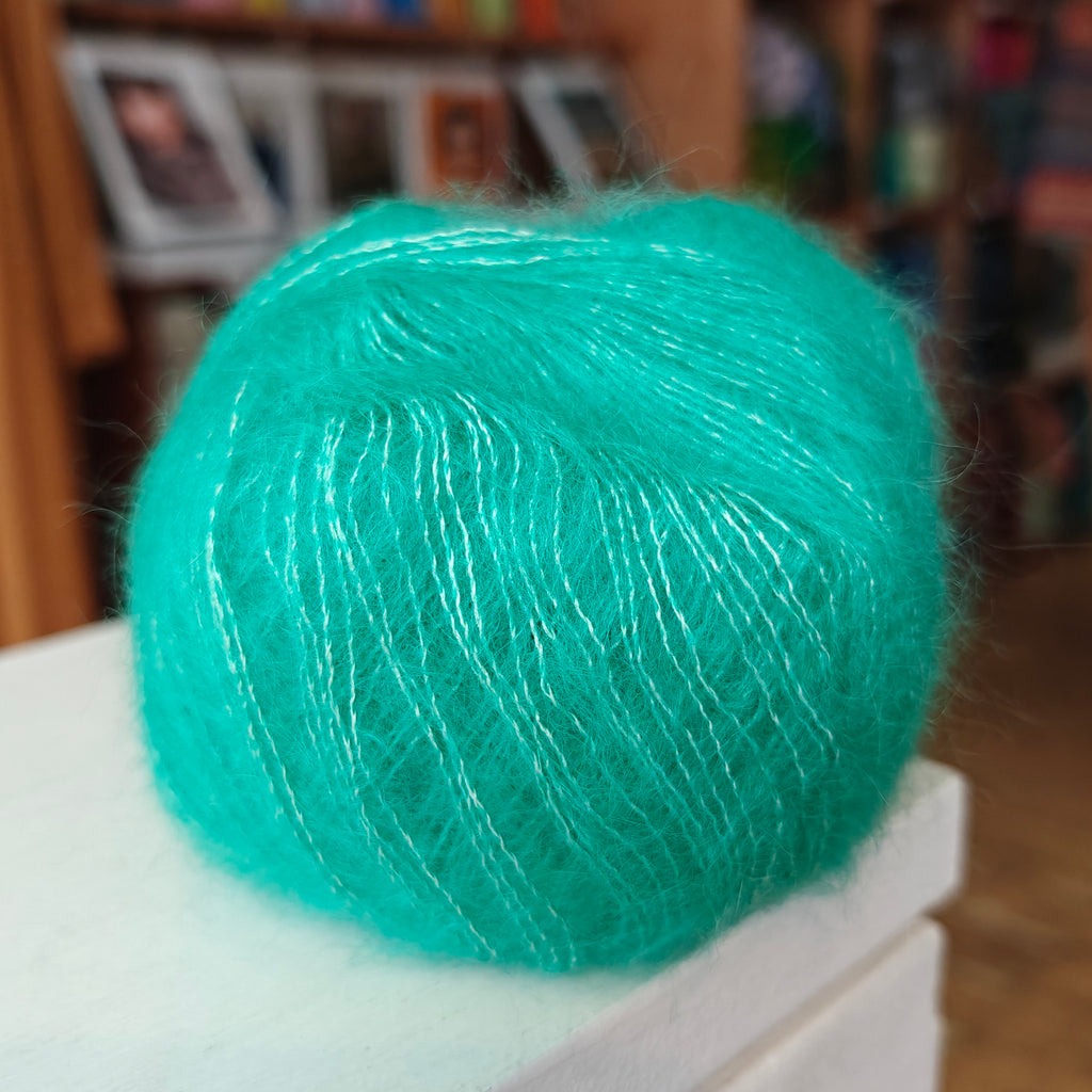 Turquoise yarn ball on a white surface with a blurred background