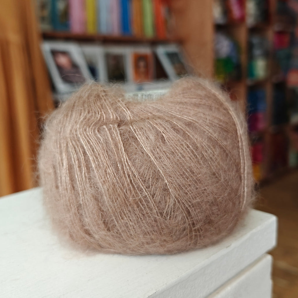 Ball of brown yarn on a white surface with a blurred bookshelf in the background