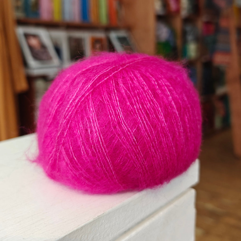 Pink yarn ball on a white surface with a blurred bookshelf background