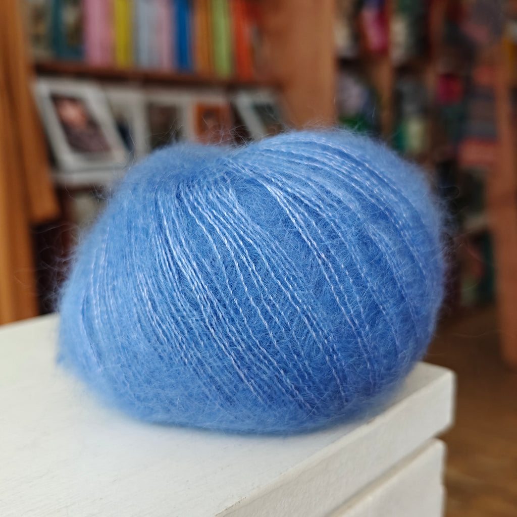 Blue yarn ball on a white surface with a blurred bookshelf background