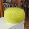 Yellow yarn ball on a white surface with a blurred bookshelf background