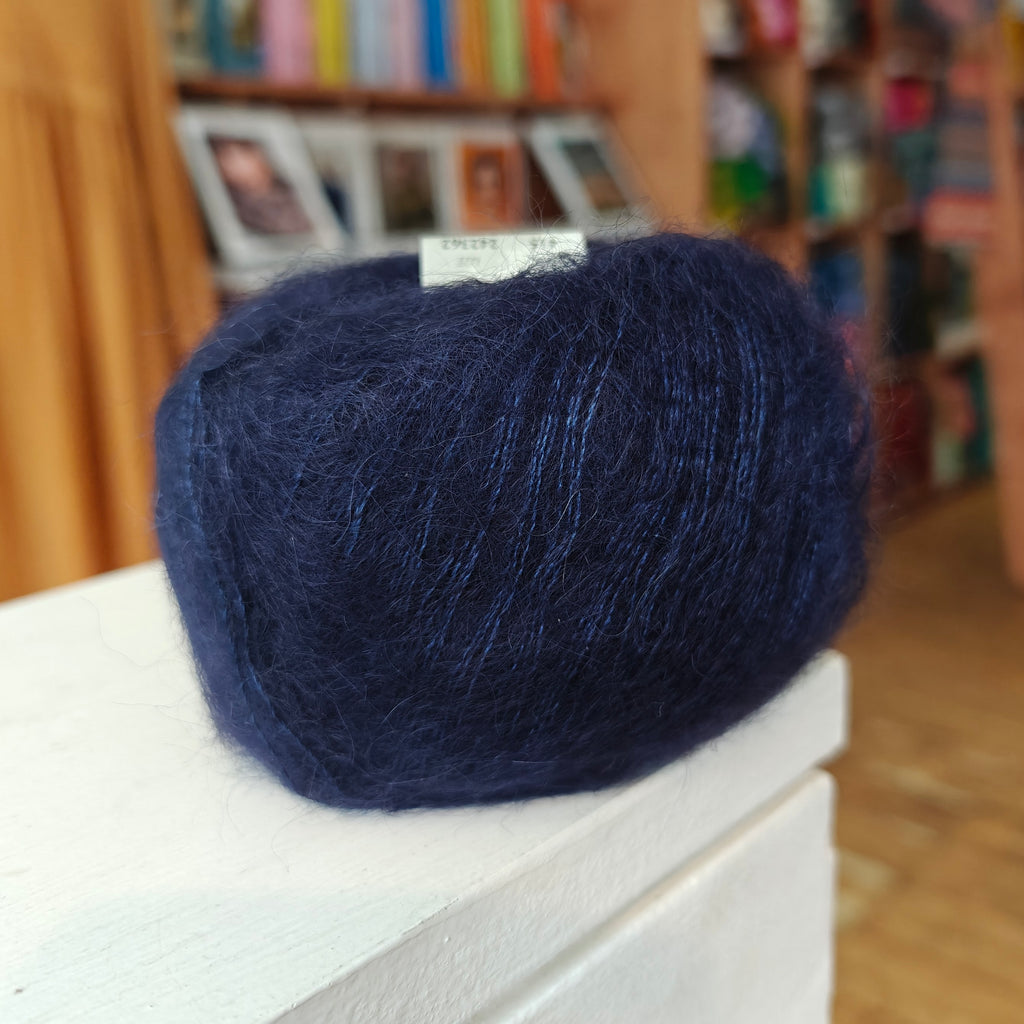 Blue yarn ball on a white surface with a blurred bookshelf background