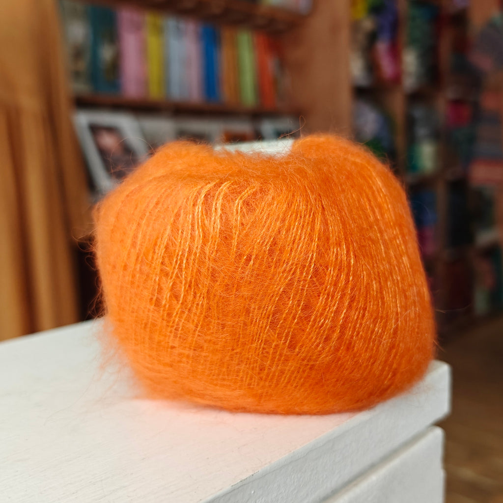 Orange yarn ball on a white surface with a blurred bookshelf background