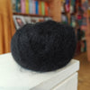 Black yarn ball on a white surface with a blurred bookshelf background