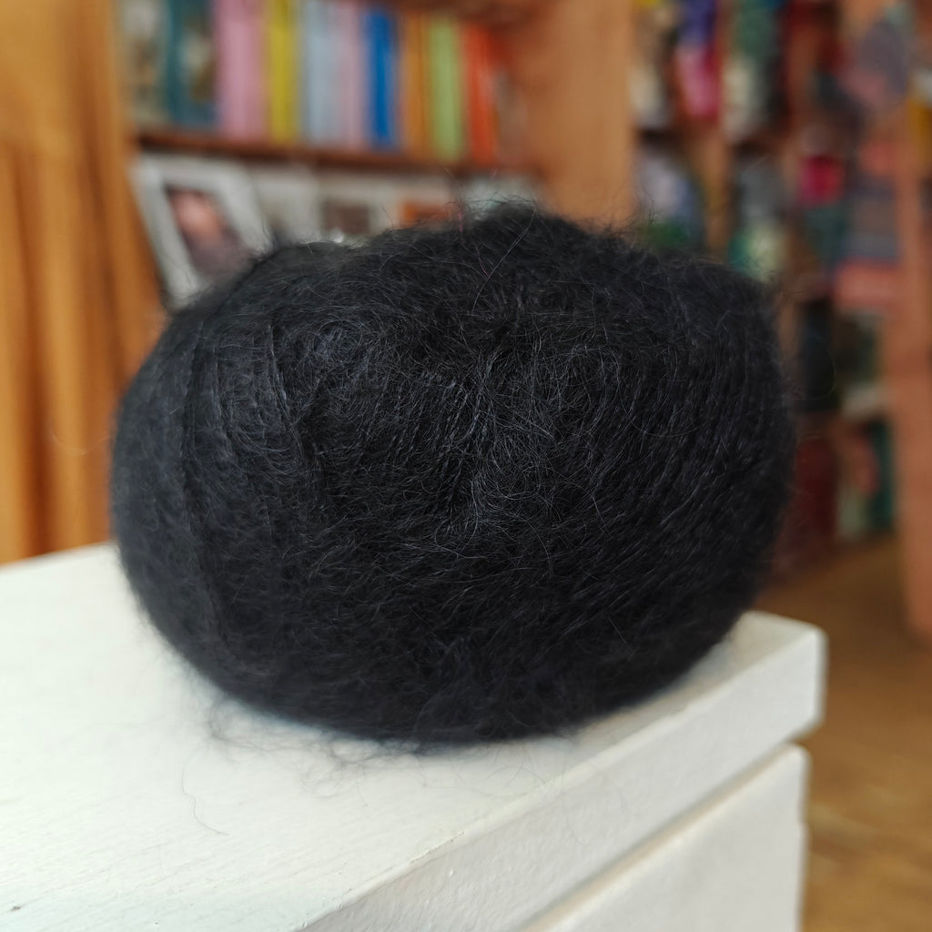Black yarn ball on a white surface with a blurred bookshelf background