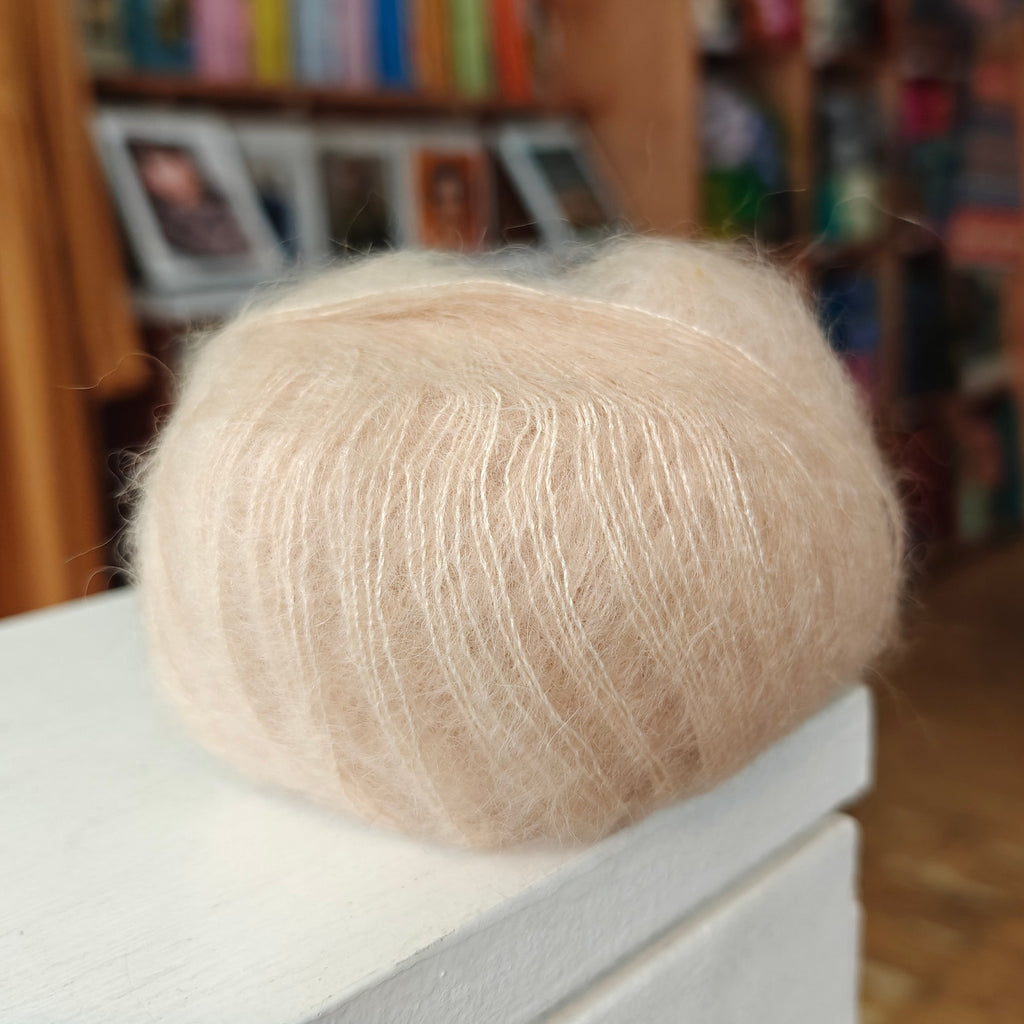 Ball of beige yarn on a white surface with a blurred bookshelf background