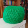 Green yarn on a white surface with a blurred bookshelf background