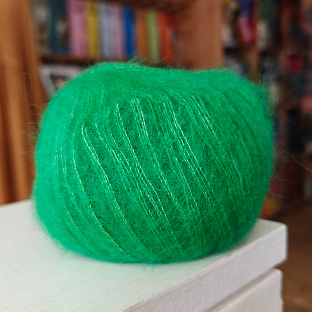Green yarn on a white surface with a blurred bookshelf background