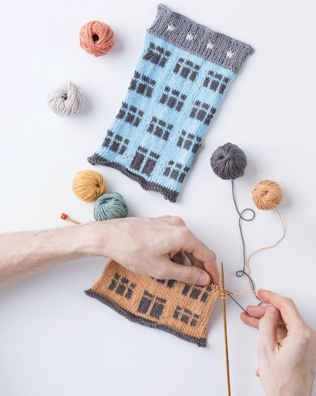 Person knitting a patterned sock with yarn and needles on a white background