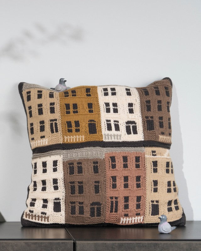 Crocheted pillow with building pattern on a wooden surface