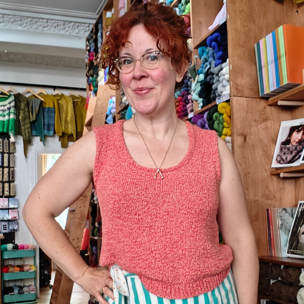 Woman in a pink sleeveless top standing in a store with shelves and products in the background
