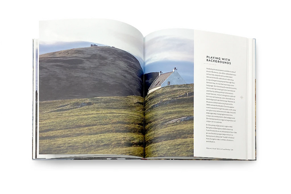 Open book showing a landscape image on one page and text on the other, with a house on a hill.