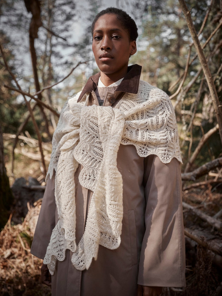 Person wearing a beige coat with a white lace shawl in a forest setting