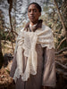 Person wearing a beige coat with a white lace shawl in a forest setting