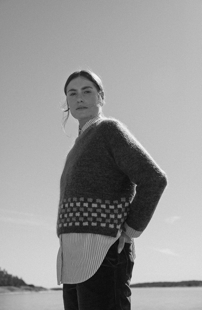 Person wearing a patterned sweater standing on a beach with a plain background