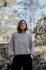 Person wearing a gray sweater in a forest setting