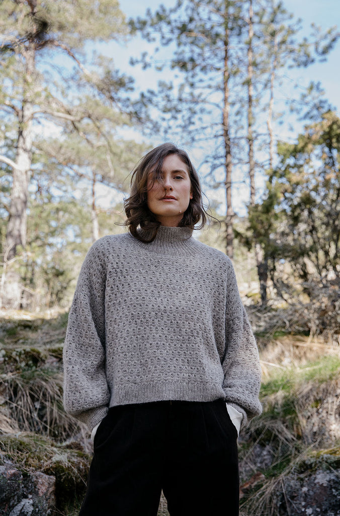 Person wearing a gray sweater in a forest setting
