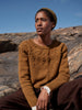 Person wearing a brown knitted sweater sitting on rocky terrain with blue sky.