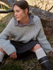 Woman sitting outdoors wearing a cable knit sweater and dark pants.