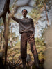 Person wearing a patterned sweater and brown pants standing in a forest.