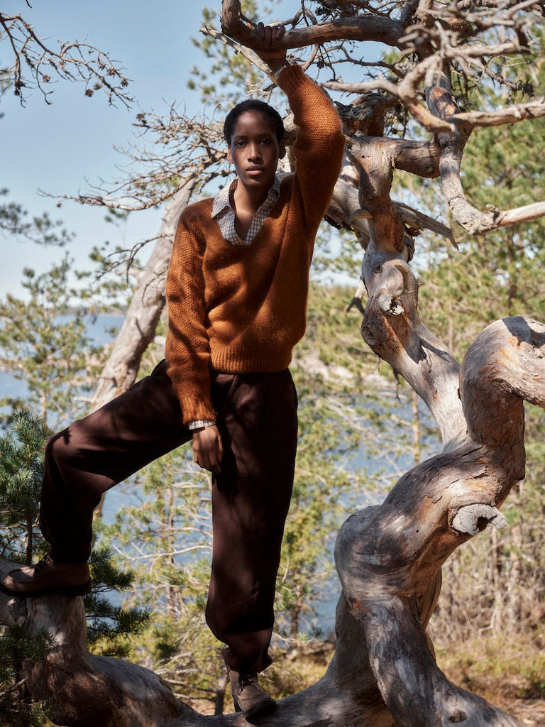 Person in a brown sweater and pants standing on a log in a forest setting