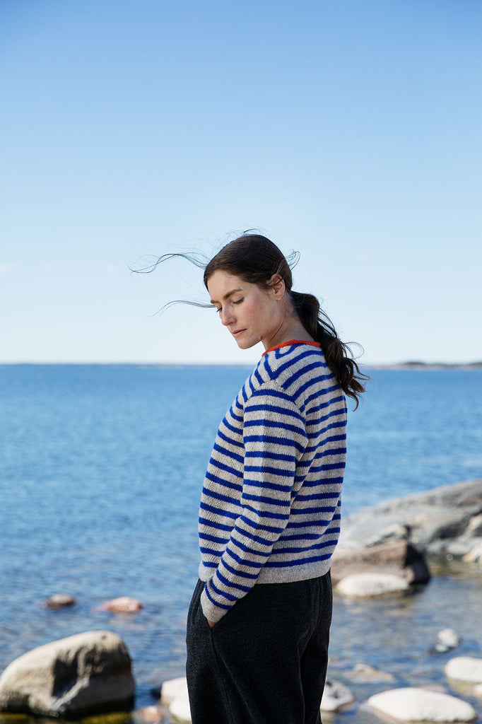 Woman in a striped sweater standing by the sea with clear blue sky
