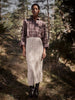 Person wearing a plaid shirt and knitted skirt standing in a forest