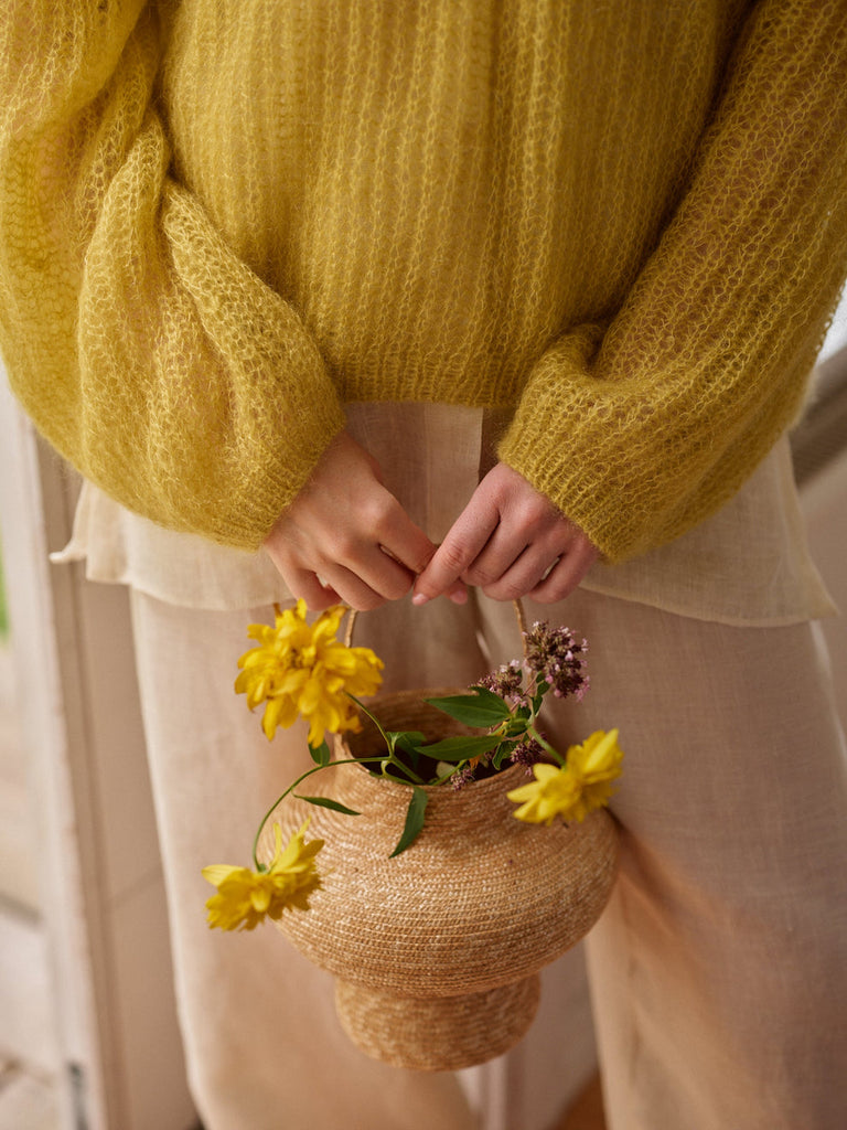 Person wearing a yellow sweater holding a woven basket with yellow flowers.