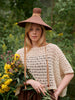 Woman wearing a wide-brimmed hat and holding flowers in a natural setting