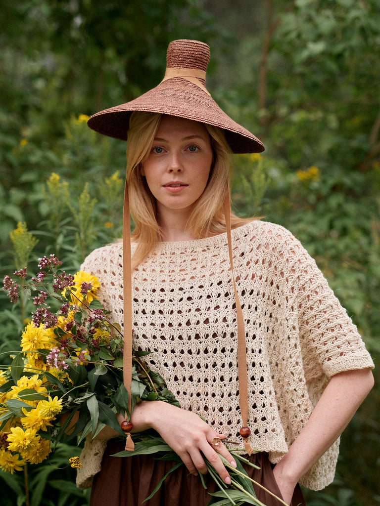 Woman wearing a wide-brimmed hat and holding flowers in a natural setting