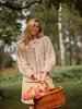 Woman in a beige cardigan holding a basket with flowers in a forest setting