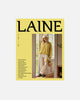 Magazine cover with a person in a yellow sweater and white pants, featuring the brand 'Laine'.