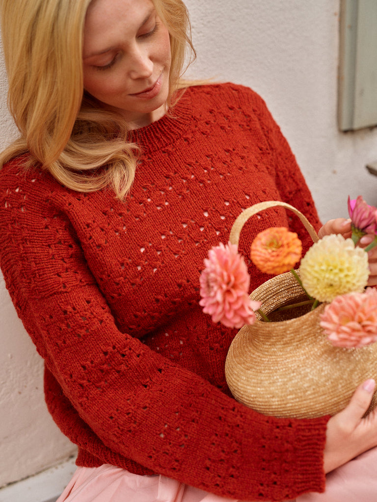Woman in a red sweater holding a woven basket with flowers against a light background