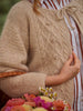 Person wearing a beige cable knit sweater with a blurred background