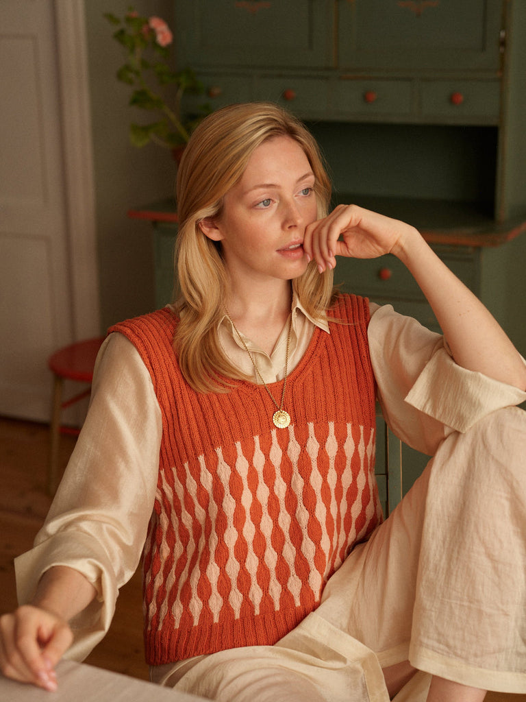 Woman wearing a red patterned vest sitting indoors.