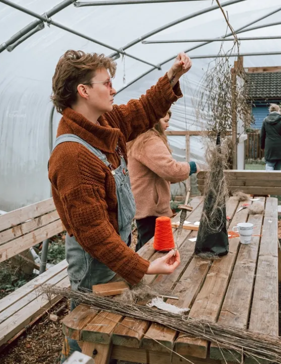 Person in a brown jacket working with yarn in a greenhouse setting