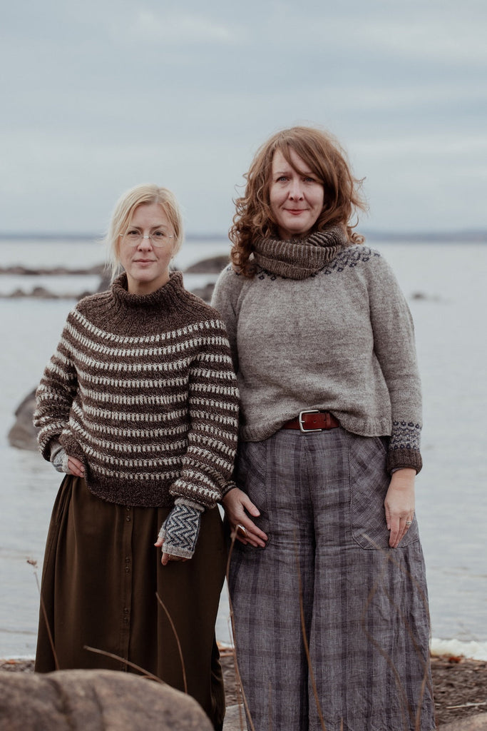 Two women standing on a beach wearing patterned sweaters and plaid skirts.