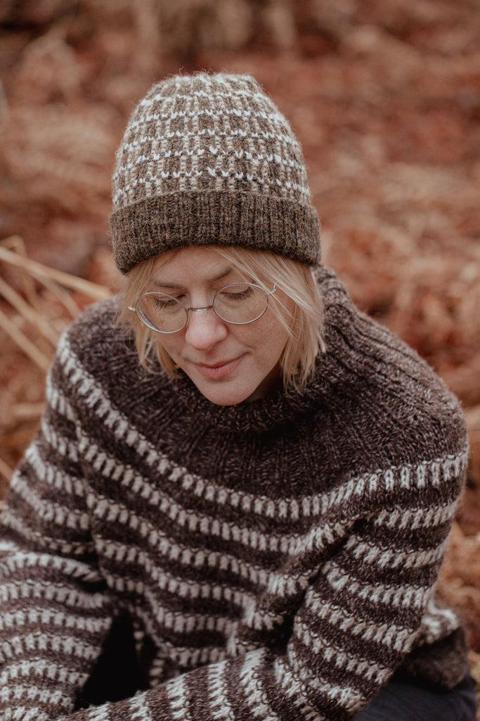 Person wearing a brown and white patterned sweater and hat in a natural setting.