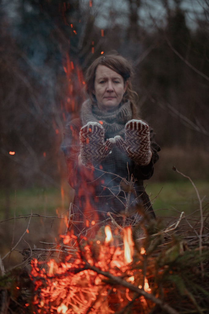 Person wearing mittens by a campfire in a natural setting