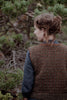 Person wearing a patterned vest standing in a forest setting