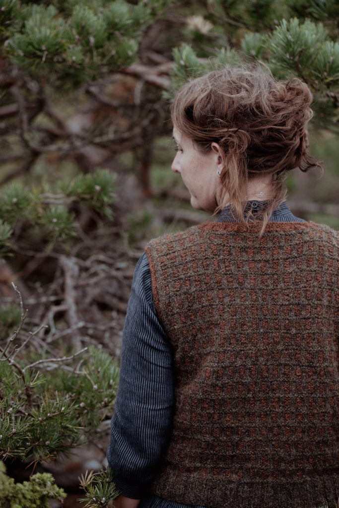 Person wearing a patterned vest standing in a forest setting