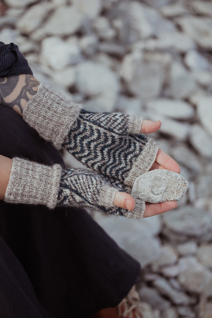Person wearing knitted fingerless gloves with a pattern against a rocky background