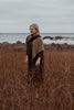 Woman standing in a field of tall brown grass with a body of water in the background