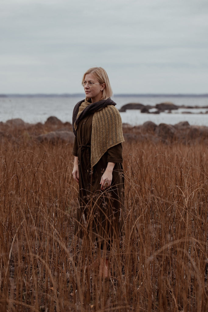 Woman standing in a field of tall brown grass with a body of water in the background
