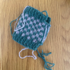 A small hand-knitted drawstring pouch in teal and white, laid flat on a light brown wooden surface.