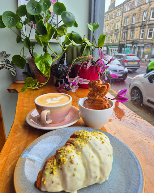 Café setting with a cup of coffee, a pastry, and decorative elements on a wooden table.