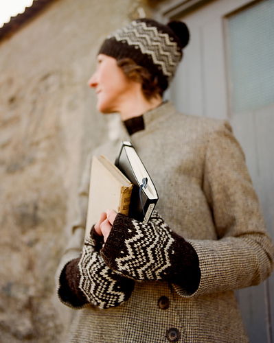 Person wearing a patterned hat and mittens holding books outdoors.