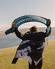 Person holding a green knitted shawl over their head with a scenic background